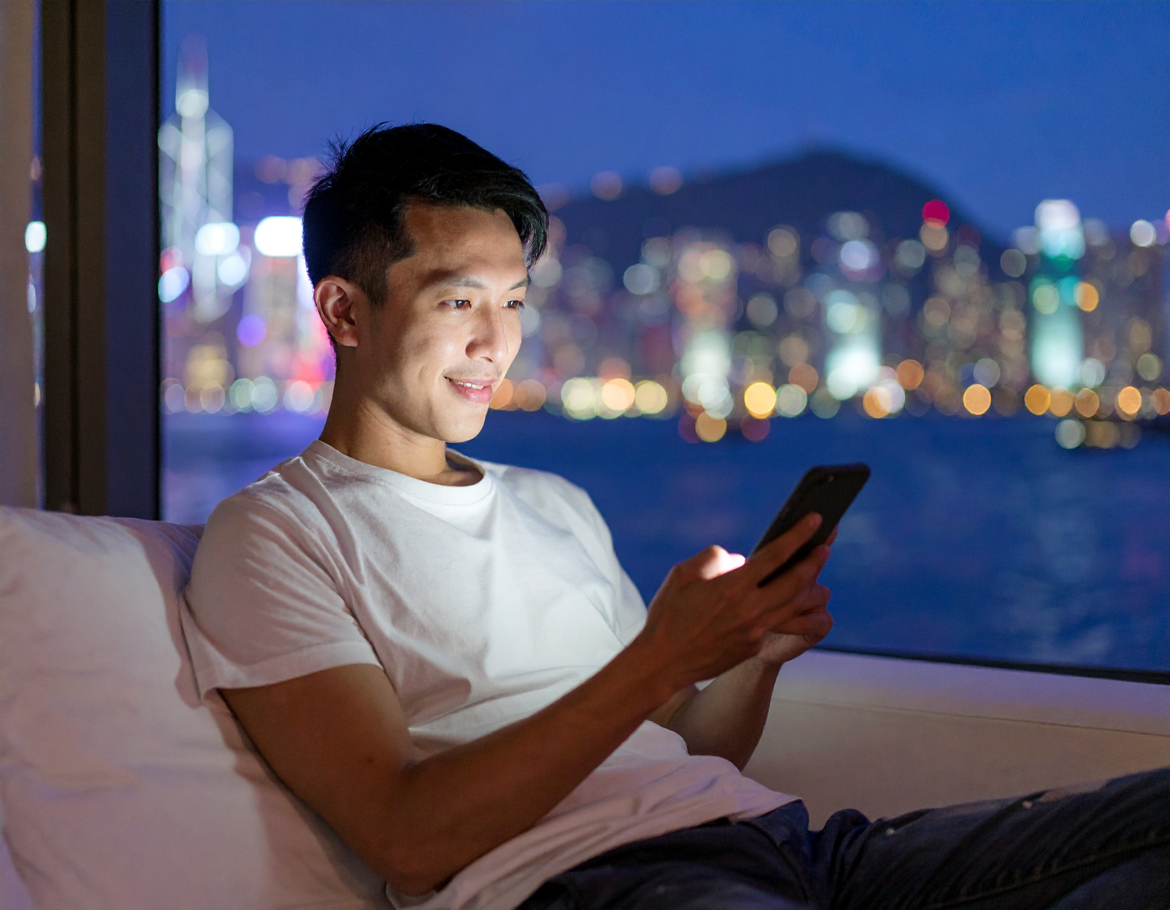 Jeune homme souriant, assis utilisant son smartphone